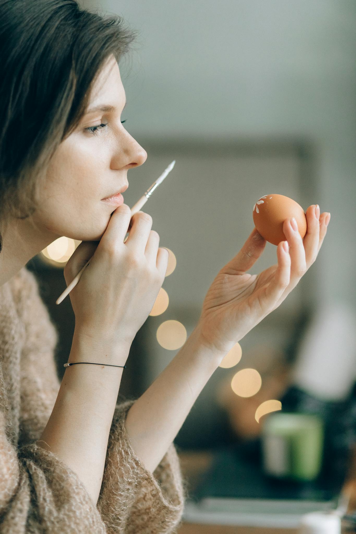 Artistic side view of a woman painting an Easter egg with focus on creativity.